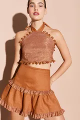 Top halter de lino con acabado brillante, presenta un diseño con escote alto y detalles de mini ojalillos decorativos en los bordes. Posee espalda descubierta con ajuste mediante lazo al cuello.