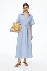 Vestido midi con diseño a rayas en tonos azul y blanco, cuello camisero, botonadura frontal y mangas raglán cortas. Cuenta con elástico fino en la parte posterior de la cintura y tira para atar extraíble.