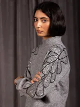 Buzo de cuello alto color gris, de manga larga, con detalle de bordado floral con lentejuelas en el hombro y parte superior de la manga.