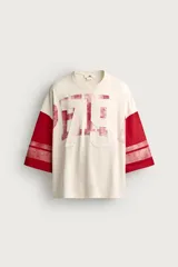 Camiseta boxy fit de cuello redondo y manga por debajo del codo. Presenta un diseño bicolor en tonos blanco off-white y rojo, con estampado y parches frontales con efecto lavado vintage y franjas en las mangas.