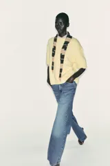 Jersey de punto color amarillo pálido, con cuello redondo y mangas cortas. Presenta un calce oversize y aberturas caladas en los laterales inferiores.