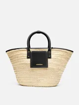 Bolso tipo canasto Jacquemus Le Panier Soli tejido en fibra vegetal de color natural, con asas cortas, detalles y bolsillo frontal de cuero negro con el logotipo de la marca en letras doradas.