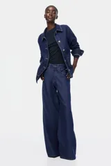 Campera camisera de denim azul oscuro con cuello, cierre frontal de botones, hombros caídos, mangas largas con puños abotonados y dos bolsillos delanteros de parche.