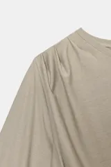 Top asimétrico color beige, con cuello redondo, una manga sisa y una manga larga abullonada. Presenta detalles de pliegues en el frente.