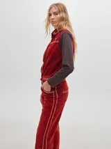 Chaleco de pana negro con cierre frontal de botones metálicos dorados. Presenta detalles de costuras en contraste en el cuello, cartera y canesú, e incluye un pequeño parche con forma de bandera en el pecho.