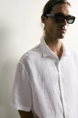 Camisa regular fit confeccionada en tejido de lino, color blanco, con cuello solapa, manga corta y cierre frontal de botonadura.