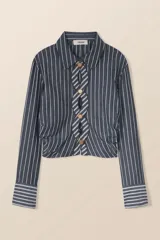 Camisa corta a rayas verticales grises y blancas, con cuello clásico y mangas largas. Presenta un diseño trenzado en el frente con botones dorados y aberturas.