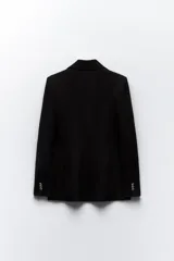 Blazer de corte entallado con cuello y solapa, manga larga y hombros marcados. Presenta un cierre frontal cruzado con botones dorados y bolsillos delanteros con solapa.