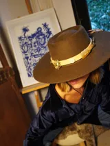 Sombrero de fieltro color marrón con ala ancha y cinta de cuero con apliques metálicos.