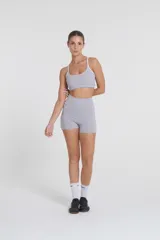 Top deportivo gris con tirantes blancos regulables, escote medio y compresión media. Confeccionado con tejido Activelu con nula transparencia.