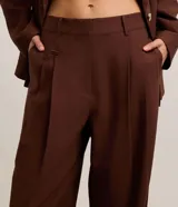 Pantalón wide leg de sastrería y cintura alta en color marrón, confeccionado en mezcla de viscosa y lino, con pliegues frontales y trabillas para cinturón.