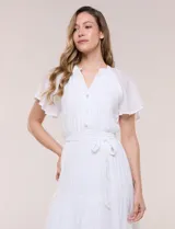 Vestido midi blanco de calce suelto y caída fluida, con escote en V, cuello a la base y apertura abotonada con detalle de puntilla. Cuenta con cintura elastizada con lazo para anudar a tono, mangas cortas con volados y falda con volantes escalonados.