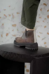 Bota tipo chelsea de punta redonda, confeccionada en una combinación de cuero texturizado y gamuza en tonos marrones. Presenta elásticos laterales negros y una suela track robusta de goma negra.