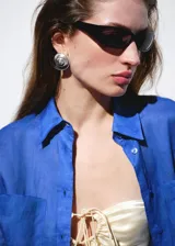 Camisa de ramio color azul eléctrico, de corte recto y largo, con cuello camisero, manga larga con puños abotonados, dos bolsillos de parche en el pecho y cierre frontal con botones.
