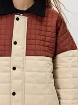 Campera acolchada de diseño colorblock, con el pecho y hombros en tono bordó y el cuerpo y mangas en color beige. Presenta cuello camisero y puños de pana negra, cierre frontal oculto con botones a presión y costuras pespuntadas en patrón cuadriculado.