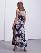 Vestido largo de seda fría con estampado floral en tonos beige y blanco sobre fondo azul marino. Tiene cuello redondo cruzado con abertura y aplique metálico.