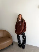 Buzo de corderito color marrón, con cuello alto y cierre frontal parcial. Presenta un diseño holgado con mangas largas y un parche decorativo en el frente.