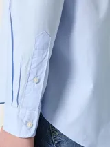 Camisa celeste de popelina de algodón flexible, con cuello abotonado, cierre con botones, puños con botones y logo de Tommy Hilfiger bordado en el pecho.