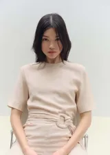 Mono largo de diseño recto, color beige, con cuello redondo, mangas cortas y cierre de botón en la parte posterior. Incluye un cinturón integrado con hebilla del mismo tejido para ajustar a la cintura.