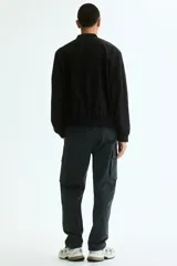 Campera bomber liviana color negro, con cuello, puños y dobladillo acanalados, cierre frontal metálico y bolsillos laterales ribeteados.