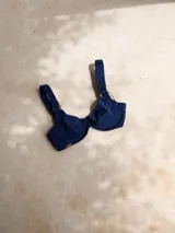 Top de bikini con aros, confeccionado en tela brillante color azul oscuro. Presenta breteles regulables con argollas decorativas y cierre mediante atado en la espalda.