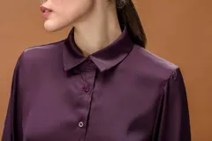 Camisa de seda color violeta oscuro, con cuello clásico, cierre frontal de botones y mangas largas con puños abotonados.