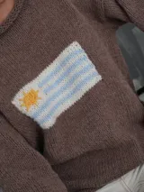 Sweater tejido a mano de color azul marino con diseño de la bandera de Uruguay en el centro del frente. Presenta un calce relajado, cuello redondo y terminaciones simples en puños y dobladillo.