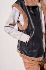 Chaleco negro de cuero sintético con interior de piel sintética color beige, cierre frontal con cremallera y corte oversize.