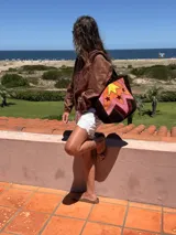 Bolso tote artesanal de cuero, reversible. Un lado presenta un diseño patchwork con figuras geométricas delimitadas por pasamanería en tonos tierra, naranja, amarillo y rosado. El reverso es liso.