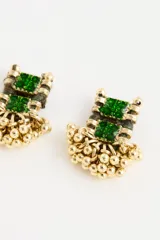 Aro de estilo étnico con piedra rectangular verde central, engarzado en metal dorado y decorado con pequeñas cuentas colgantes en la base.