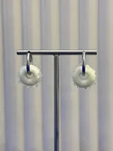 Aros tipo argolla con dije de vidrio en forma de dona color blanco, con textura de pequeñas esferas de vidrio alrededor. Base de plata 925.