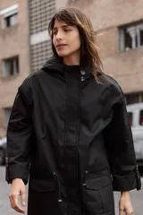 Parka liviana color beige con capucha, cierre frontal con botones, bolsillos delanteros con tapa y ajuste en la cintura. Presenta mangas con puños vueltos y detalle de botones.
