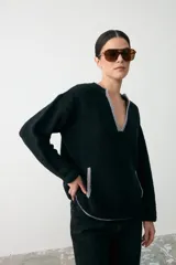Sweater de textura bouclé color negro con detalles de ribete en color gris en el escote en V, puños y bolsillos frontales. Presenta un diseño de manga larga y corte holgado.