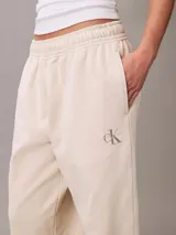 Pantalón tipo jogger de Calvin Klein en color beige, confeccionado en tejido de felpa de mezcla de algodón. Presenta cintura elástica con cordón ajustable, bolsillos laterales y bajos con puños de canalé. Incluye un discreto monograma de la marca estampado en la pierna.