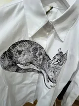 Camisa blanca de algodón con cuello clásico, manga larga con puños abotonados y estampado frontal de un animal similar a un zorro.
