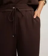 Pantalón de vestir femenino color marrón oscuro, de corte fluido y tiro medio/alto, con cintura elástica ajustable mediante cordón. Presenta bolsillos laterales y cierre frontal.
