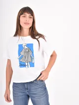 Remera blanca de algodón con cuello redondo y mangas cortas. Presenta un estampado frontal con pinceladas de colores y la frase 'in love we trust'.