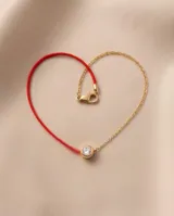 Pulsera de hilo rojo de seda combinada con cadena de acero con baño de oro, con un dije redondo central tipo punto de luz engastado con circorias.