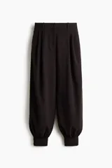 Pantalón negro de corte holgado con diseño de piernas globo, pinzas en la cintura y puños ceñidos en los tobillos.