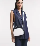 Bolso pequeño de cuero sintético blanco, con forma redondeada, correa larga ajustable y cierre de cremallera.