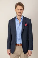 Saco de vestir azul marino, confeccionado en lana, con solapas clásicas, cierre frontal de dos botones y bolsillo en el pecho con pañuelo decorativo.