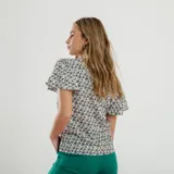 Blusa blanca con estampado de flores azules y verdes, cuello redondo con abertura en forma de gota y mangas cortas amplias.