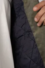 Chaqueta de estilo militar color verde oliva, confeccionada en gabardina resistente. Presenta cuello camisero en contraste color negro, cierre frontal con cremallera, dos bolsillos frontales tipo cargo con solapa y ajuste relajado.