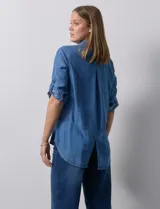 Camisa gris de tencel con cuello con solapa, escote en V y abertura central con botones. Largo de manga regulable con presilla y botón. Ruedo en espalda con tajo.