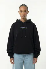 Hoodie negro de corte relajado con capucha y bolsillo canguro frontal. Presenta una estampa artística de alto impacto en la espalda con motivos digitales y gráficos de estilo retro-futurista en tonos violeta, verde y blanco.