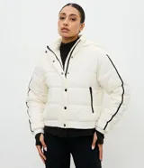 Campera puffer deportiva Get Over, color blanco con detalles de bies en color negro a lo largo de las mangas. Presenta cuello alto con capucha integrada, cierre frontal con botones a presión, bolsillos laterales con cremallera y puños con elásticos.