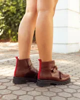 Botinetas de cuero color marrón con suela track negra. Presentan un cierre frontal con detalle en color rojo, dos correas con hebillas metálicas ajustables y puntera redondeada.