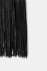 Vestido largo negro de tejido elástico, con escote halter y bajo con flecos a tono.