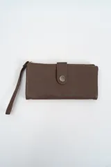 Billetera rectangular de cuero sintético con textura granulada, color marrón. Cuenta con cierre de solapa con botón a presión metálico y correa de muñeca extraíble.