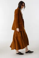 Falda midi de gamuza color marrón, con diseño de corte amplio, tajo lateral y cintura con elástico en la parte trasera. Cuenta con cierre metálico lateral y forro interior.